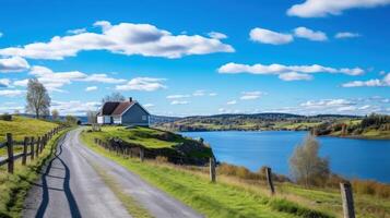 A scenic road winds through a rural landscape, leading to a quaint house perched on a hill overlooking a sparkling lake. photo