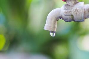 Close-Up of a Dripping Water Faucet Against a Green Blurred Background in Natural Light photo