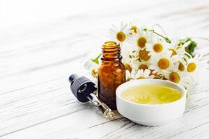 aromatic chamomile essential oil on a white wooden rustic background photo