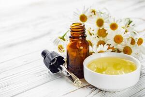 aromatic chamomile essential oil on a white wooden rustic background photo