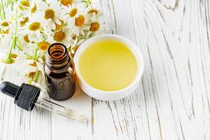 aromatic chamomile essential oil on a white wooden rustic background photo