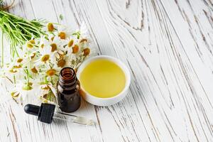 aromatic chamomile essential oil on a white wooden rustic background photo