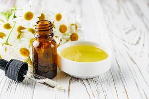 aromatic chamomile essential oil on a white wooden rustic background photo