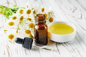 aromatic chamomile essential oil on a white wooden rustic background photo
