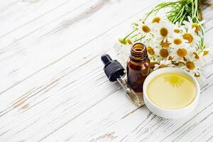 aromatic chamomile essential oil on a white wooden rustic background photo