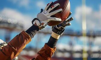 A football player's hands catching the ball mid-air, with the field and goalposts in the background photo