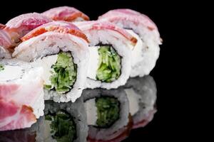 sushi roll with cream cheese cucumber bacon on a black mirror background photo