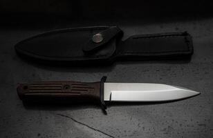 A modern hunting knife and a leather case for him on a dark background. Melee weapons for hunting and self-defense. The instrument of crime. photo