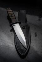 A modern hunting knife and a leather case for him on a dark background. Melee weapons for hunting and self-defense. The instrument of crime. photo