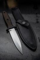 A modern hunting knife and a leather case for him on a dark background. Melee weapons for hunting and self-defense. The instrument of crime. photo