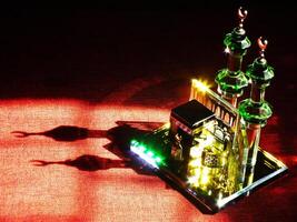 Small model of the Kaaba, the holy mosque of the Grand Mosque, Mecca, isolated on a dark background. There is sunlight coming performing an amazing shadow and shining reflection photo