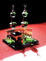 Small model of the Kaaba, the holy mosque of the Grand Mosque, Mecca, display at the top of red fabric material and dark background. There is sunlight coming from behind to form an amazing reflection photo