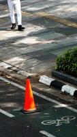 A person is walking on the sidewalk next to a cone sign and cyclist icon. The person only seems by the feet photo