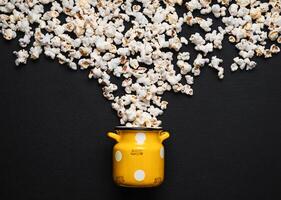 popcorn on a dark background, pouring out of a yellow can with white polka dots photo