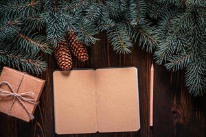 Christmas frame from fir branches on a background of an old brown board around an open notebook with blank sheets. Frame of fir branches. Christmas card blank concept. photo