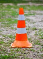 Orange road cone with white stripes on a back of green grass. photo
