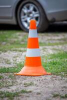 Orange road cone with white stripes on a background of green grass. A car in the back. photo