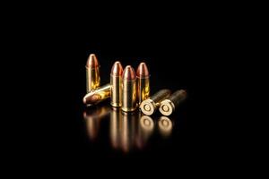 Pistol cartridges 9 mm on a smooth glossy surface with reflections. Ammunition for pistols and PCC carbines on a dark back. photo