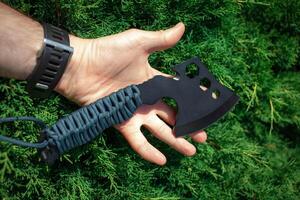 A small black ax with a paracord-wrapped handle. A tool for cutting branches or firewood in the forest. Self defense weapon. Green back. photo