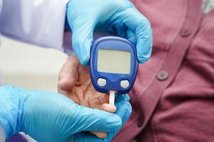 Asian doctor using digital glucose meter for check sample blood sugar level to treatment diabetes. photo