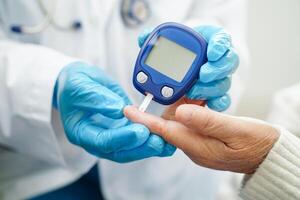 Asian doctor using digital glucose meter for check sample blood sugar level to treatment diabetes. photo