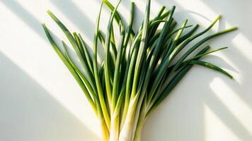 Bunch spring green onions are placed on white table. Lighting is coming from side. photo