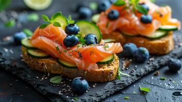 Fresh salmon on grain bread. Decorated with cucumbers, blueberries and herbs. Appetizer on a black background. Ideal for restaurants, menus and culinary blogs. Combination of textures and colors. photo