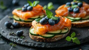 Fresh salmon on grain bread. Decorated with cucumbers, blueberries and herbs. Appetizer on a black background. Ideal for restaurants, menus and culinary blogs. Combination of textures and colors. photo