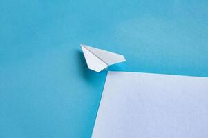 Angle view of paper airplane flying on blue background with customizable space for text photo