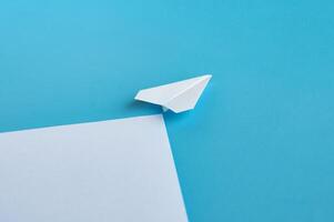 Angle view of white paper airplane flying along the route on blue background with customizable space for text photo