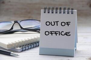 Out of office text on white notepad with notes and glasses background photo