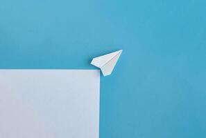 Angle view of white paper airplane flying along the route on blue background with customizable space for text photo