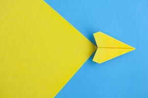 Top view of yellow paper airplane flying on blue background with customizable space for text photo