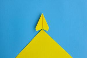 Top view of yellow paper airplane flying along the route on blue background with customizable space for text photo