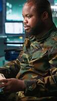 Vertical Military soldier in mission control center overseeing national safety operations, reading folder files. African american army specialist checking data in monitoring room command center, camera A video