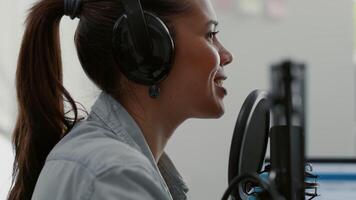 Attractive talk show host broadcasting while talking to audience in home studio. Internet famous star speaking at microphone to public while recording podcast in living room. video