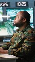 Vertical Military agent working in control room, analyzing aerial reconnaissance data and talking with colleague. Intelligence corps agent checking screens, discussing with coworker, camera A video