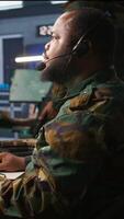 Vertical Military dispatcher relays info from army intelligence analysts to troops on front lines, close up shot. Radio communications operator wearing uniform talking in headset mic, camera B video