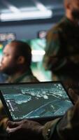 Vertical Army telecommunication systems operator using satellite software on tablet, providing combat support. Military dispatcher managing communications networks, with portable device, camera B video