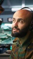 Vertical Middle Eastern military dispatcher relays info from army intelligence analysts to troops on front lines, close up. Radio communications operator discussing with colleague using headset mic, camera B video