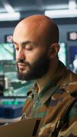 Vertical Military soldier in mission control center answering telephone call, overseeing national safety operations. Army specialist talking on phone, examining data in monitoring room, camera B video