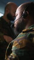 Vertical Military dispatcher using headphones microphone, offering information to commanders fighting on front lines. Army expert providing intel for troops in base of operations, camera A video