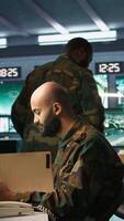 Vertical Military officer in command post receiving telephone call while looking at intel files. Intelligence specialist reading opponents strategy mission case file and talking on phone, camera B video