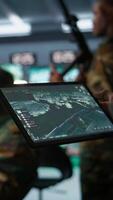 Vertical Military agent working in control room, using software on tablet, analyzing aerial reconnaissance data. Close up of intelligence corps expert controlling drones with portable device, camera B video