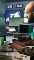 Vertical Military soldier in mission control center overseeing national safety operations with devices, close up. Middle Eastern army specialist examining data in monitoring room command center, camera B video