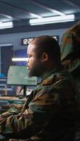 Vertical Officer in command center helped by colleague to plan, analyze and gather information on enemy troops. Team of agents in base of operations doing assessment of adversaries vulnerabilities, camera B video