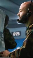 Vertical Military dispatcher using headphones microphone, offering info to infantry units fighting on front lines. Army expert providing intel for troops, coordinating mission activities, camera A video