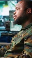 Vertical Military agent working overtime in control room to analyze aerial reconnaissance data, feeling tired. Exhausted intelligence corps agent controlling drones, suffering from headache, camera A video