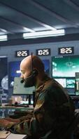 Vertical Army telecommunication systems operator using radio and satellite equipment. Middle Eastern military dispatcher managing communications networks, looking at screens, camera B video