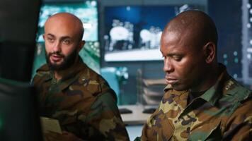 Army unit working in governmental facility next to coworker, doing brainstorming, operating surveillance tech. Team of soldiers doing job in HQ base of operations, camera A video
